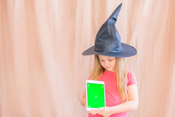 Retrato de una chica en un sombrero de bruja con una maqueta verde pantalla de la tableta espacio de copia de Halloween —  Fotos de Stock