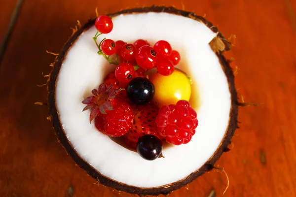 Kırmızı ve siyah üzümlü üzümler, ahududular, çilekler, kirazlar gün ışığında kahverengi ahşap bir masada hindistan cevizinin içinde yatıyor..