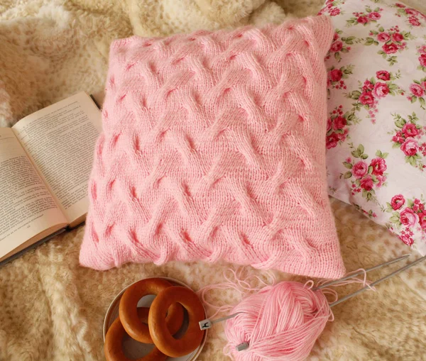 Açık bir kitabın yanında açık pembe bir yastık, açık bir kitap, örgü iğneli iplik, hamur işleriyle dolu bir tabak. Dikiş konsepti.