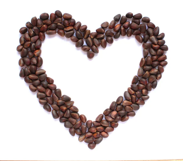Beyaz arka planda izole edilmiş kalp şeklinde çam fıstıkları.