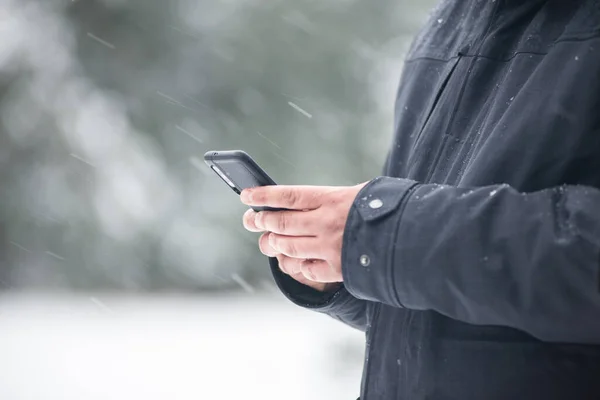 Close up of the hands of a Caucasian man typing on his mobile phone while it snows.Copy space