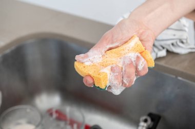 Kirli bardak kovasının üzerinde sabun köpüğü ile el temizleme pedini kapat. Temiz konsept.