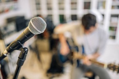 Stüdyo mikrofonunu kaydediyorum. Odaklanamayan bir arka planda gitar çalan genç bir adam. Müziğin tadını çıkarın.