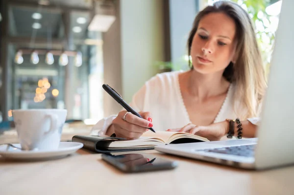 Young businesswoman writing in her notebook in a coffee shop.Focus on the hand and notebook