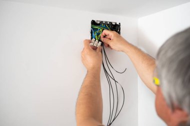 Elektrikçi beyaz bir duvardaki kabloları tamir ediyor. Küçük profesyonel iş adamı konsepti..