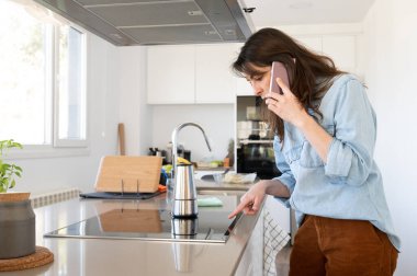 Busy working woman talking on the phone and preparing coffee in her kitchen at home