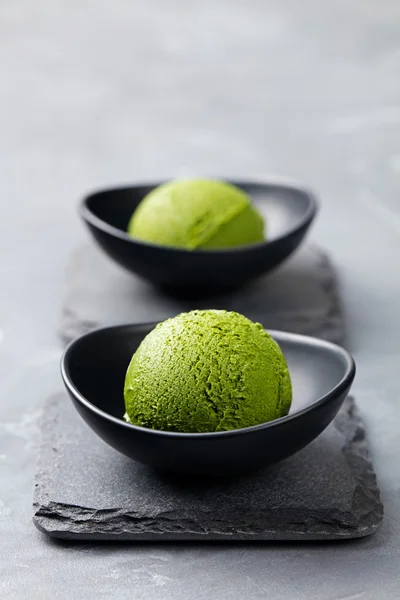 Green tea matcha ice cream scoop in bowl on a grey stone background. Copy space