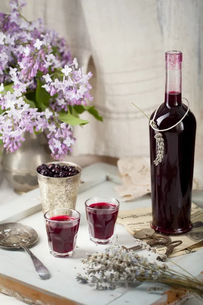 Blackcurrant homemade liquor with lilac flowers. Wooden background