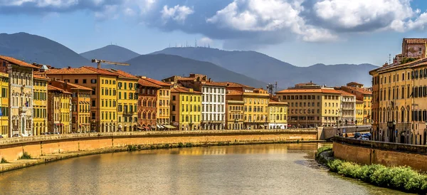 Pisa 'nın içinden akan Arno Nehri, arkasında dağlar olan renkli binalarla çevrili.