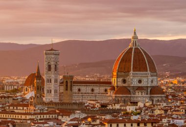 Floransa 'nın güzel Gotik katedrali gün batımında arka planda dağlarla birlikte çevre şehir binalarının üzerinde duruyor.