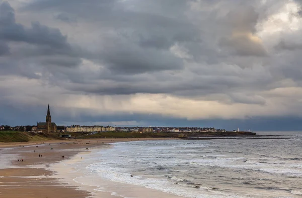 İngiltere 'nin kuzeydoğusunda, bulutlu ve yağmurlu bir günde Tynemouth' un Longsand plajında yürüyüş yapan insanlar.