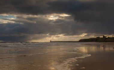 İngiltere 'nin kuzeydoğusunda, bulutlu ve yağmurlu bir günde Tynemouth' un Longsand plajında yürüyüş yapan insanlar.