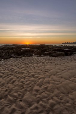 Tynemouth 'un Longsand plajında güneş ufukta görünürken kayaların üzerinde