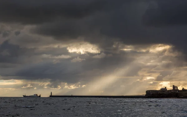 Crepuscular, bulutlu bir günde İngiltere 'nin kuzeydoğusundaki Tynemouth, Tarikat ve rıhtım üzerinde parlıyor.