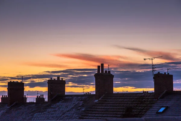Gün batımında çatıların üzerinde canlı bir gökyüzüne karşı siluet yapılmış baca kapları.