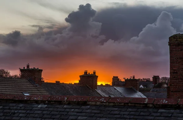 Buz kaplı çatı kiremitleri ve bacalar ve bir şehir sahnesinde gün doğumu