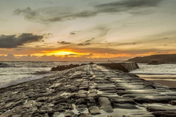 İngiltere 'nin kuzeydoğusunda serin bir Cullercoats Körfezi' nde gün doğumu, uzakta Tynemouth İskelesi ve deniz feneri.