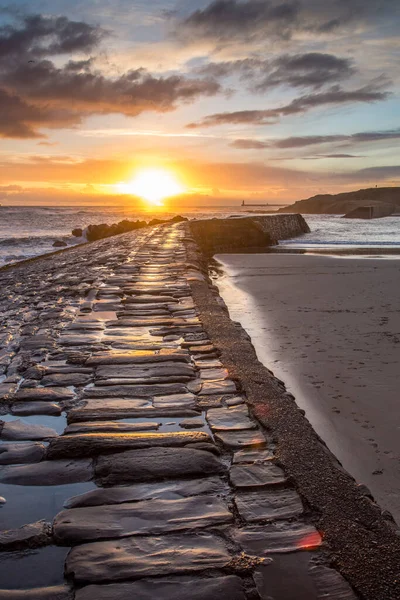 İngiltere 'nin kuzeydoğusunda serin bir Cullercoats Körfezi' nde gün doğumu, uzakta Tynemouth İskelesi ve deniz feneri.