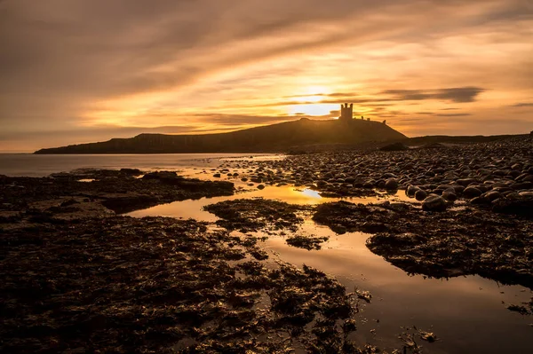 Dunstanburgh Şatosu 'nun en güzel gündoğumu Northumberland' daki meşhur kaygan kayalarla gökyüzü renklerle dolup taştı.