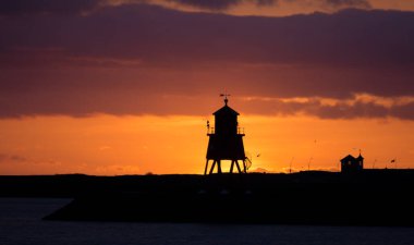 Güney Shields 'deki eski, kırmızı, ahşap Herd Groyne Deniz Feneri, bulutlu bir sabahta güneşin doğuşuyla siluete büründü.