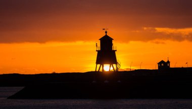 Güney Shields 'deki eski, kırmızı, ahşap Herd Groyne Deniz Feneri, bulutlu bir sabahta güneşin doğuşuyla siluete büründü.