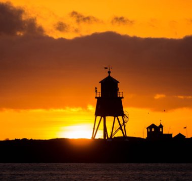 Güney Shields 'deki eski, kırmızı, ahşap Herd Groyne Deniz Feneri, bulutlu bir sabahta güneşin doğuşuyla siluete büründü.