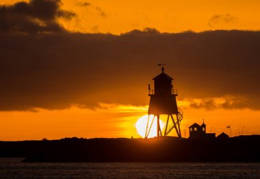 Güney Shields 'deki eski, kırmızı, ahşap Herd Groyne Deniz Feneri, bulutlu bir sabahta güneşin doğuşuyla siluete büründü.
