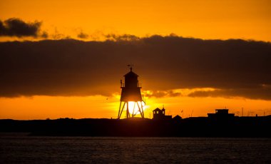 Güney Shields 'deki eski, kırmızı, ahşap Herd Groyne Deniz Feneri, bulutlu bir sabahta güneşin doğuşuyla siluete büründü.