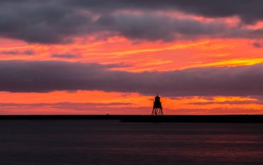 Güney Shields 'deki eski, kırmızı, ahşap Herd Groyne Deniz Feneri, bulutlu bir sabahta güneşin doğuşuyla siluete büründü.