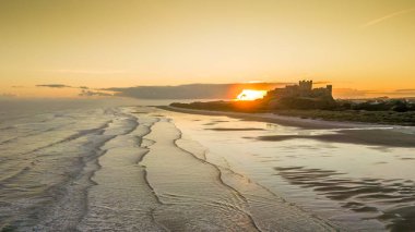 Güneş doğarken dondurucu soğuk bir sabahta Northumberland, İngiltere 'de karla kaplı kumsalın yanında insansız hava aracı tarafından çekilen ikonik Bamburgh Şatosu..