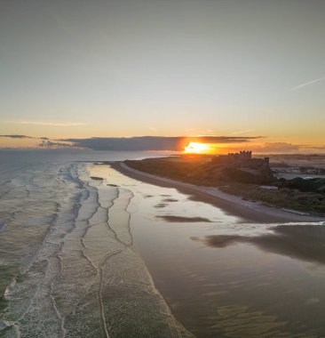 Güneş doğarken dondurucu soğuk bir sabahta Northumberland, İngiltere 'de karla kaplı kumsalın yanında insansız hava aracı tarafından çekilen ikonik Bamburgh Şatosu..