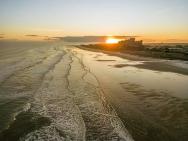 Güneş doğarken dondurucu soğuk bir sabahta Northumberland, İngiltere 'de karla kaplı kumsalın yanında insansız hava aracı tarafından çekilen ikonik Bamburgh Şatosu..