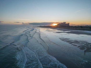Güneş doğarken dondurucu soğuk bir sabahta Northumberland, İngiltere 'de karla kaplı kumsalın yanında insansız hava aracı tarafından çekilen ikonik Bamburgh Şatosu..