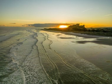 Güneş doğarken dondurucu soğuk bir sabahta Northumberland, İngiltere 'de karla kaplı kumsalın yanında insansız hava aracı tarafından çekilen ikonik Bamburgh Şatosu..