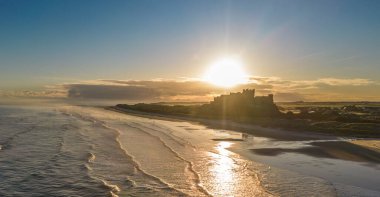 Güneş doğarken dondurucu soğuk bir sabahta Northumberland, İngiltere 'de karla kaplı kumsalın yanında insansız hava aracı tarafından çekilen ikonik Bamburgh Şatosu..