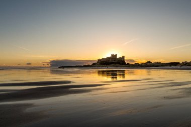 Güneş doğarken soğuk bir sabahta Northumberland, İngiltere 'de karla kaplı plajın yanındaki ikonik Bamburgh Şatosu..