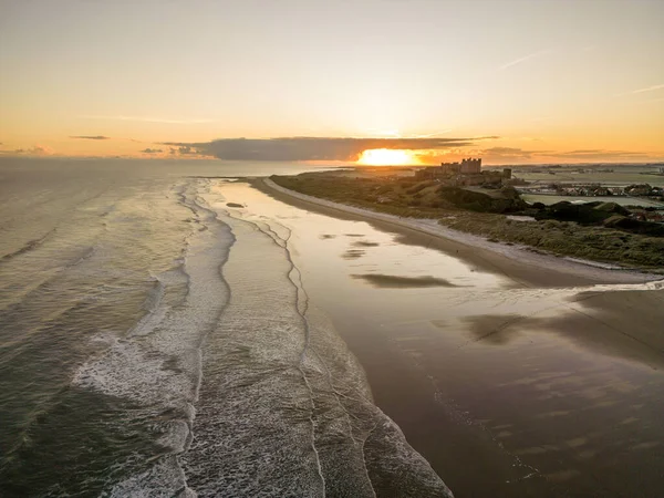 Güneş doğarken dondurucu soğuk bir sabahta Northumberland, İngiltere 'de karla kaplı kumsalın yanında insansız hava aracı tarafından çekilen ikonik Bamburgh Şatosu..