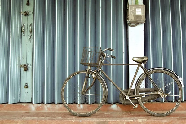 Старый велосипед стоит на красном полу возле голубых ворот Стоковое Изображение
