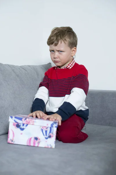 Rozrušený chlapec sedí s dárkem na posteli. Royalty Free Stock Obrázky