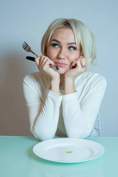 Menina sentada à mesa com uma pequena porção de comida — Fotografia de Stock