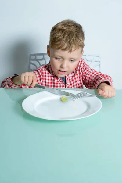 El niño se sienta a la mesa y come aguacate.. — Foto de Stock