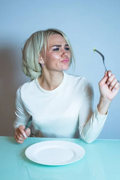 Chica enferma se sienta en la mesa y se come una verdura. — Foto de Stock