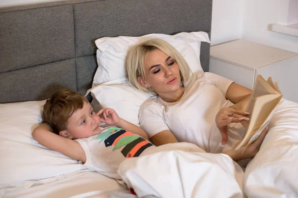 Mom reads a bedtime story to her son in bedroom.