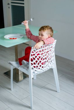 Küçük çocuk bir sandalyeye oturup sağlıklı yiyecekler yiyor..