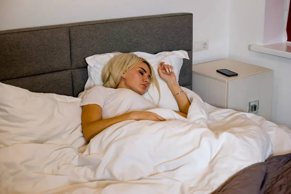 Girl sleeps in a large bed at home under blanket.