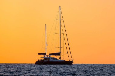 İki direkli bir yatın silueti turuncu bir gökyüzünün arka planında