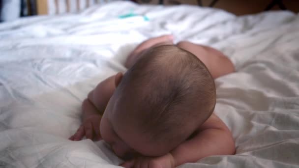 Новорожденный лежит на животе на белом простыне и пытается поднять голову. — стоковое видео