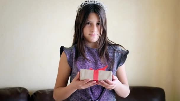 Gadis itu memegang hadiah di tangannya. Dia melihat ke kamera dan mengulurkan hadiah kepada penonton — Stok Video