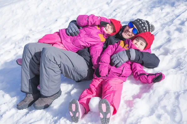 Батько і дочки розважаються лежачи на снігу — стокове фото