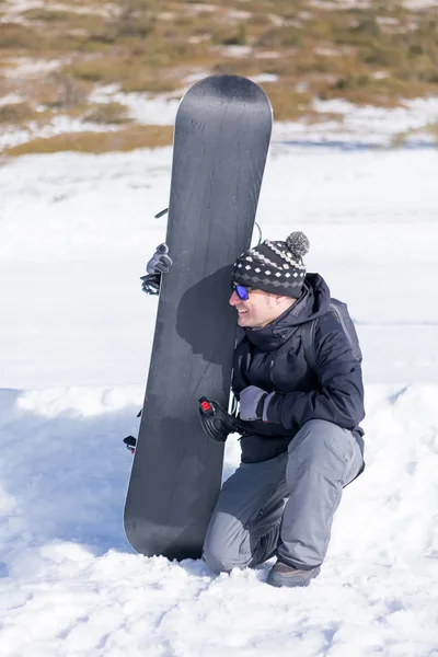 Чоловік тримає сноуборд, сидячи на одному коліні — стокове фото